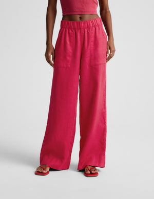 Woman wearing a red ribbed cropped tank and red linen pants against a plain background. 