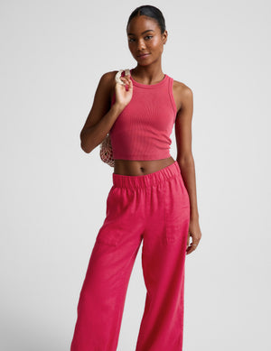 Woman wearing a red ribbed cropped tank and red linen pants against a plain background. 
