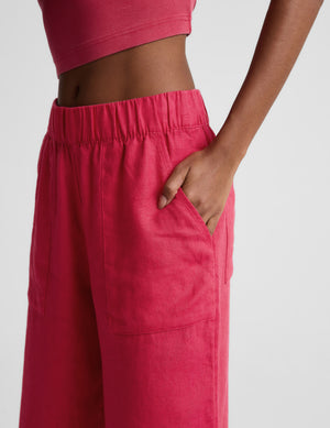 Woman wearing a red ribbed cropped tank and red linen pants against a plain background. 