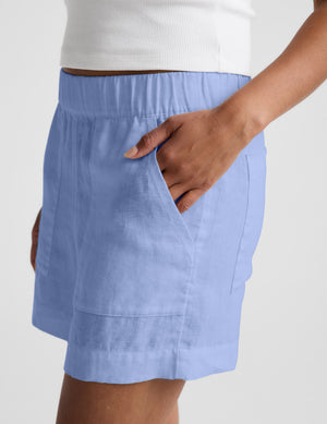 Woman wearing a white cropped t-shirt and blue linen shorts against a plain background. 