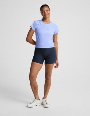 Woman wearing a light blue active short sleeve top and navy blue biker shorts against a plain background. 