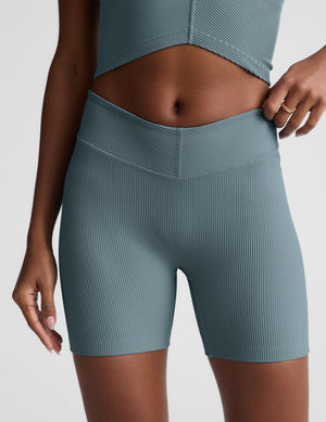Woman wearing a blue cropped tank and shorts on a light gray background. 