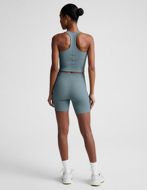 Woman wearing a blue cropped tank and shorts on a light gray background. 