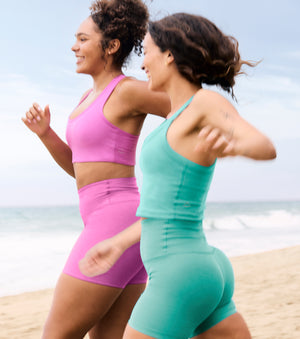 model on left is wearing a pink bra top and pink high-waisted biker shorts. model on right is wearing a blue cropped tank and blue high-waisted biker shorts. 