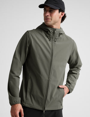 Man wearing a green jacket and black pants on a plain background. 