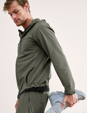 Man wearing a green jacket and shorts on a plain background. 