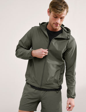 Man wearing a green jacket and shorts on a plain background. 
