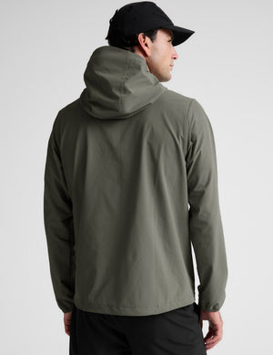 Man wearing a green jacket and black pants on a plain background. 