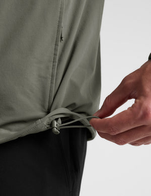 Man wearing a green jacket and black pants on a plain background. 