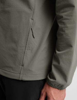 Man wearing a green jacket and black pants on a plain background. 