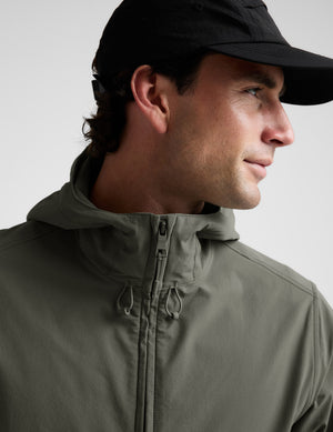 Man wearing a green jacket and black pants on a plain background. 