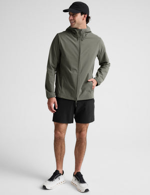 Man wearing a green jacket and black shorts on a plain background. 