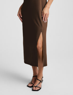 Woman wearing a brown square neck midi length dress against a plain background. 
