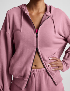 Woman wearing a pink zip-up hoodie and shorts set on a neutral background. 