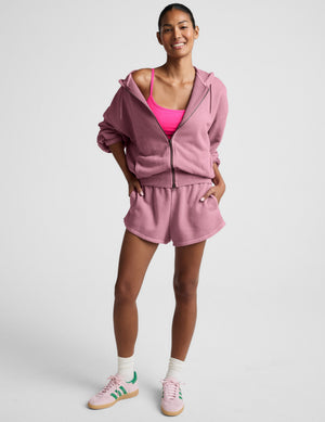 Woman wearing a pink zip-up hoodie and shorts set on a neutral background. 