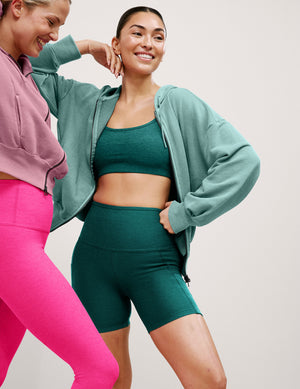 Two women in athletic wear posing against a plain background. 