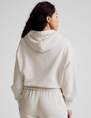 Woman wearing a white hoodie and pants against a plain background. 