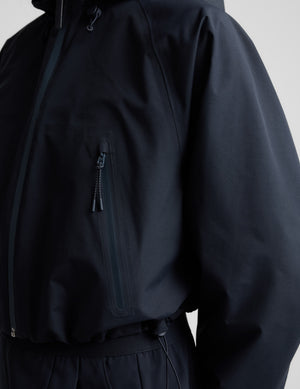 Woman wearing a blue hooded jain jacket and pants against a plain background. 