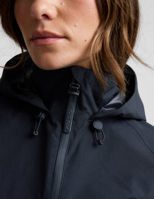 Woman wearing a blue hooded jain jacket and pants against a plain background. 