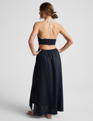 Woman wearing a navy blue halter neck midi dress on a light gray background. 