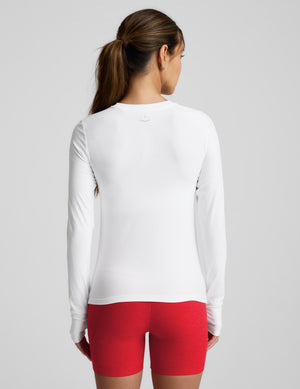 Woman wearing a white long-sleeve top and red shorts on a light gray background. 