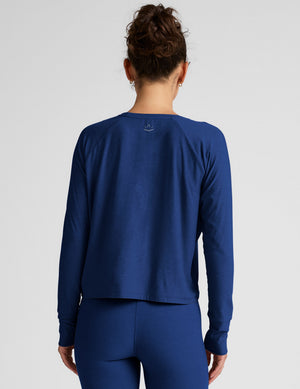 Woman wearing a blue long-sleeve top and leggings against a light background. 