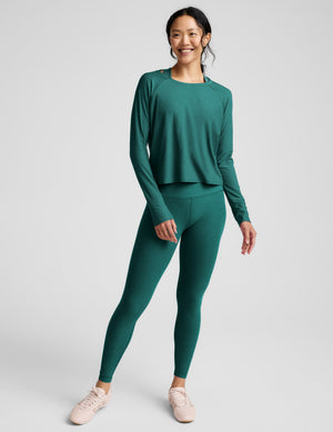 Woman wearing a teal long-sleeve top and leggings on a light gray background. 