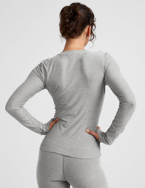 model wearing a fitted gray long-sleeve crew neck top and leggings on a light gray background. 