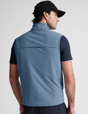 Man wearing a light blue vest over a black shirt on a plain background. 