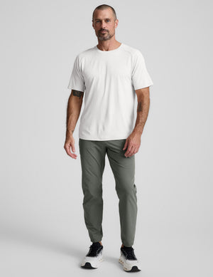 Man wearing a white t-shirt and green pants on a light gray background. 