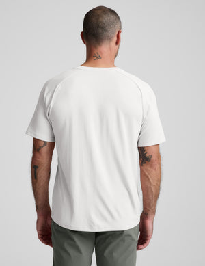 Man wearing a white t-shirt and green pants on a light gray background. 