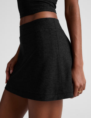 Woman wearing a black tank top and skirt with sneakers on a light gray background. 