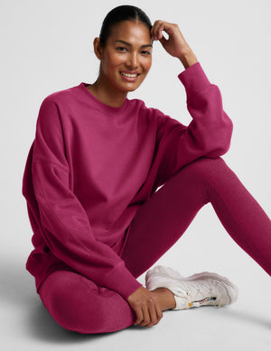 Woman wearing a red crewneck sweatshirt and leggings against a light gray background. 