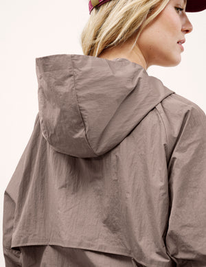 Woman wearing a brown hooded jacket and shorts on a light background. 