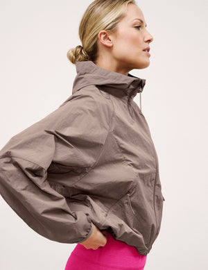 Woman wearing a brown hooded jacket on a light background. 