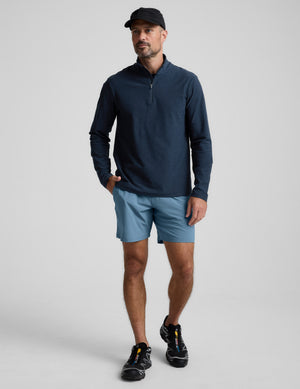 Man wearing a navy long-sleeve shirt and blue shorts on a light gray background. 