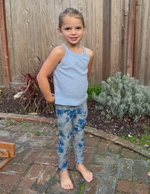 Smiling toddler girl outdoors wearing Daydream Meadow SoftMark Toddler Legging with a blue floral print on a brick patio.