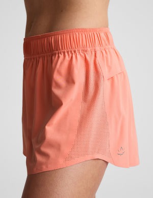 Woman wearing a coral sports bra and shorts set on a light gray background. 