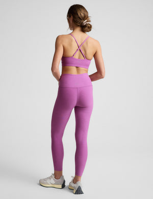 Woman wearing a purple sports bra and leggings on a light gray background. 