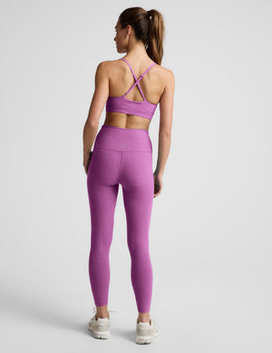 Person wearing a blue sports bra and purple leggings on a light gray background