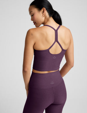 Woman wearing a purple cropped tank and leggings on a light gray background. 
