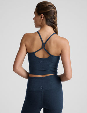 woman wearing a navy blue racerback cropped tank and leggings on a plain background. 