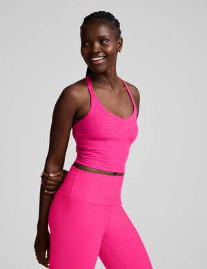 Woman wearing a pink v-neck cropped tank and leggings against a plain background. 