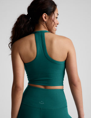Woman wearing a green cropped tank top and leggings against a plain background. 