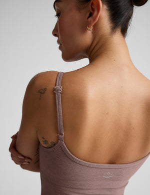 Woman wearing a brown tank top and pants against a plain background. 