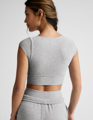 Woman wearing a gray cropped twist tee and sweatpants on a light gray background. 