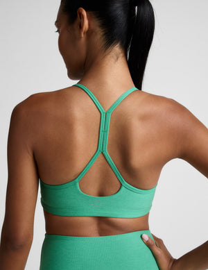 Woman wearing a green sports bra and leggings against a plain background. 