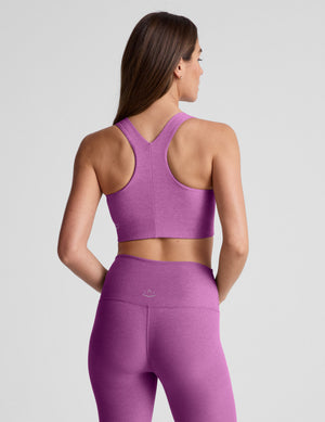 Woman wearing a purple sports bra and leggings against a plain background. 