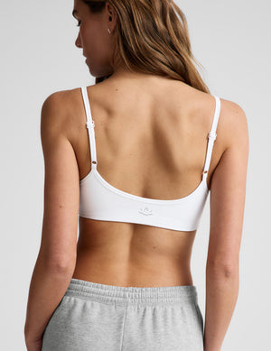 Woman wearing a white sports bra and gray sweatpants on a plain background. 