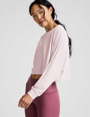 Woman wearing a pink long-sleeve top and mauve leggings indoors.